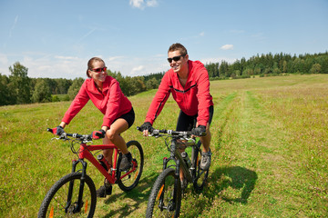 Plakat Sportive couple riding mountain bike in meadow