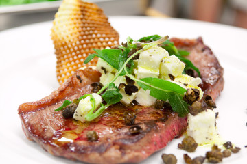 Rare cooked steak with capers and cheese topping