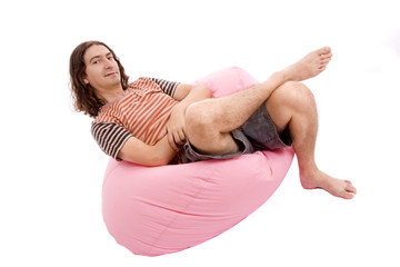 Portrait of a young casual man, seated on a pink small sofa, iso