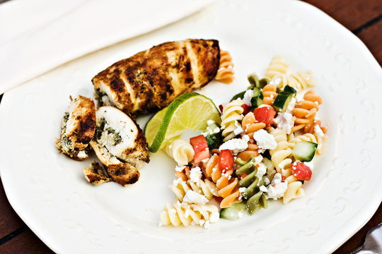 Fusilli salad served with stuffed chicken and a slice of lime.
