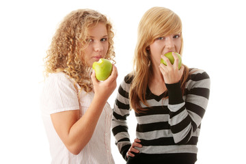 Two teen girlfriends eating green apples