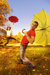 Funny couple with umbrellas on autumn background (focus on a guy