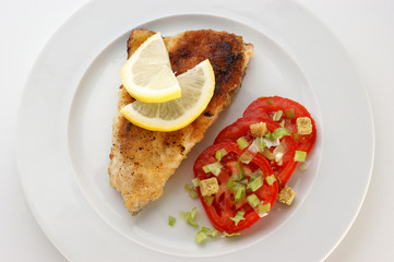 crumbed carp fillet on organic tomato on a plate