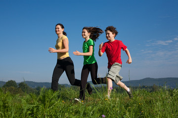 Active family - mother and kids running on green meadow