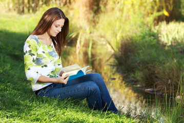 Attractive girl student reading book in autumn park.