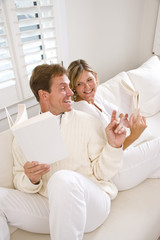 Obraz premium Couple relaxing together reading at home on white sofa