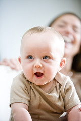 Amused six month old baby with mother laughing in background