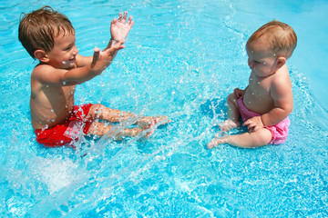 young brother and sister playing with water in pool