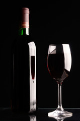 Glass and bottle of red wine on black background