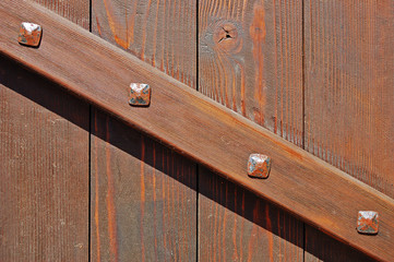 Old wooden gate with brace fastened with rusty forged bolts