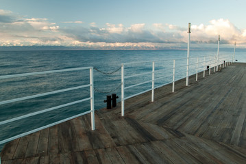 Wooden deck at the lake with mountains on the other side at sunr