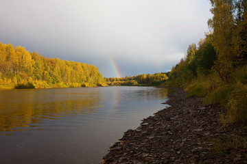 Autumn landscape. Rainbow over river in clouds