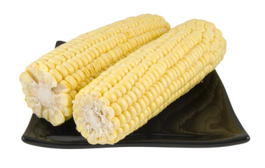 two sweetcorn cobs on black plate isolated on white
