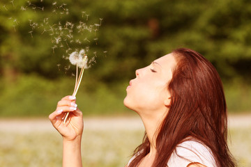 woman is blowing a dandelion