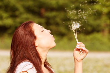 young woman ist blowing a dandelion - obrazy, fototapety, plakaty