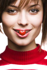 smiling young woman holding little red heart in her lips