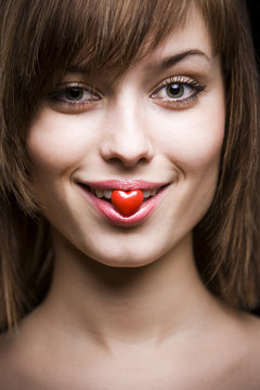 smiling nacked young woman holding little heart in her lips