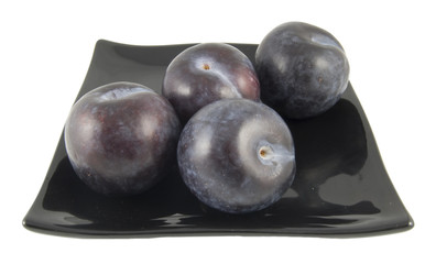 four plumbs sittin on plate isolated on white background