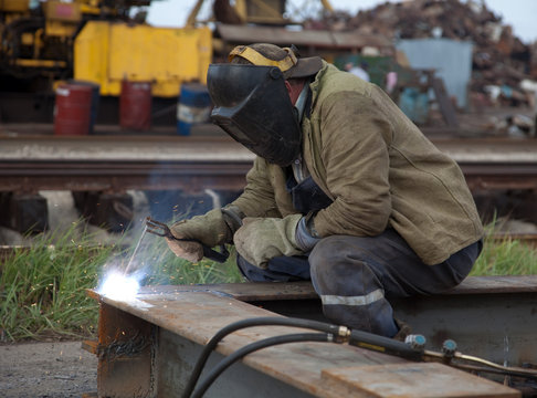 The worker- welder in a protective mask welds metal