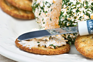 Herb cheese being spread onto a sesame cracker.