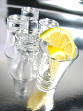 Empty shot glasses with lemon on silver background