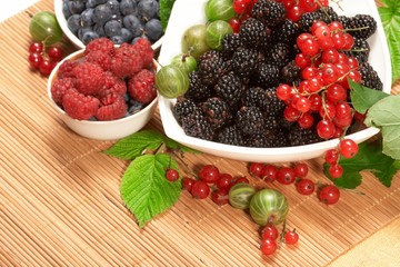 Berries in plates, on a table, among green leaves