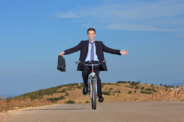 Carefree businessman holding a  briefcase and riding a bicycle