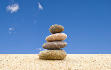 Fototapeta na wymiar The balanced stones on sand against the blue sky