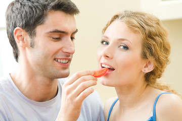 Young couple eating tomato together at home