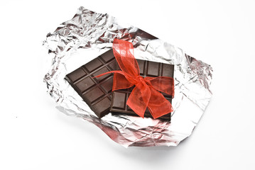 Black broken chocolate on a foil with red ribbon and bow