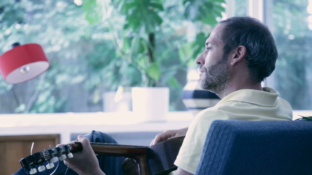 guy plays guitar in living room, relaxed