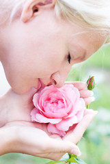 Young pretty woman enjoys a smell of  pink rose