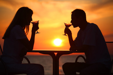 Female and man's silhouettes on sunset  drink from glasses
