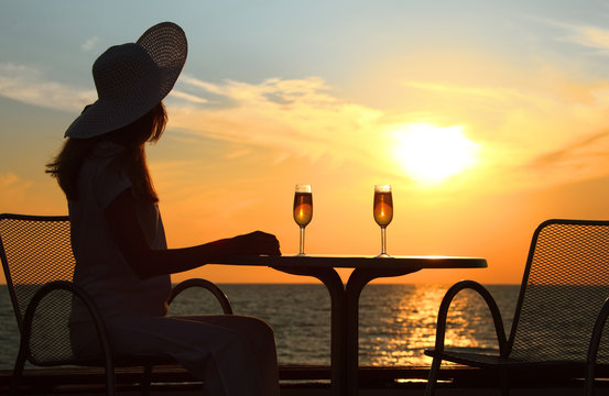 Female silhouette on sunset behind  table with two glasses