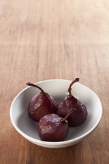 Pears poached in red wine in a white bowl.