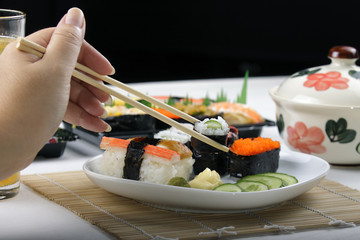 Hand holding a kappamaki from a plate of sushi