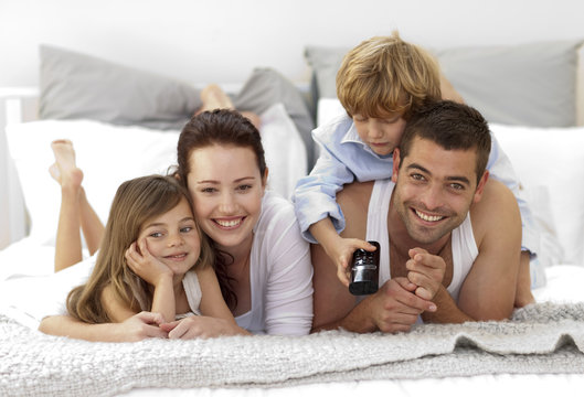 Family lying in bed watching television