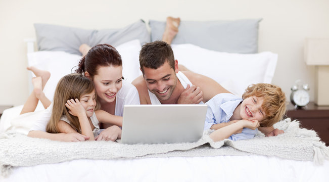 Family in bed using a laptop - Powered by Adobe