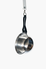 Abstract: an used saucepan hanging on a snap-hook, studio shot