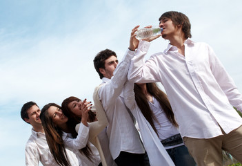 Group of young men stretching hands to a bottle with water