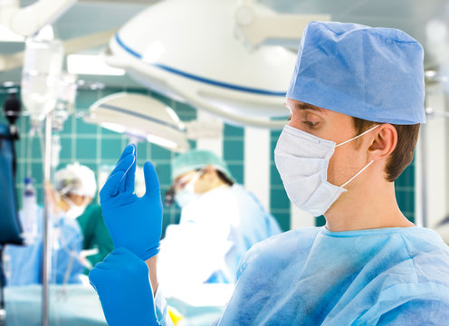 male surgeon with his team in operation room putting on gloves