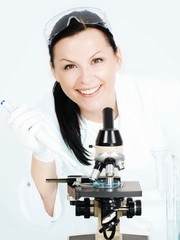 smiling brunette female researcher working on microscope in labo