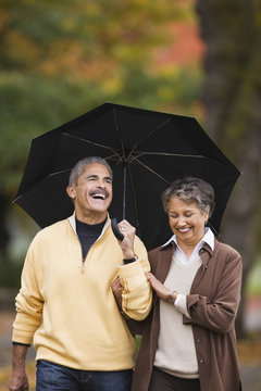 African couple walking with umbrella in autumn
