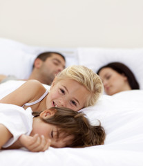 Little girl smiling wile her parents and brother sleep