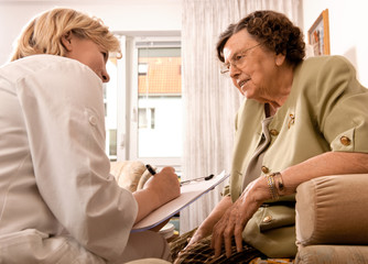 Senior woman is visited  by her doctor or caregiver at home - obrazy, fototapety, plakaty