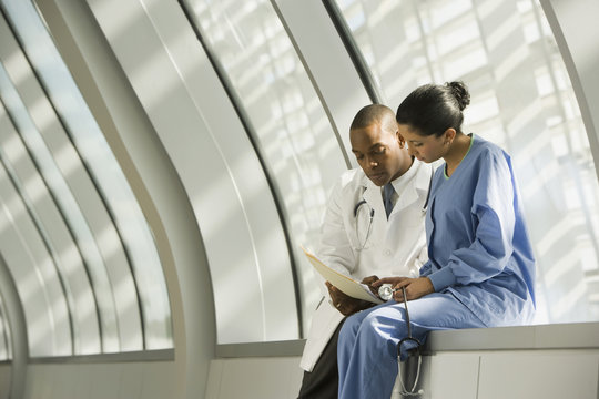 Doctor and nurse reviewing medical chart in corridor