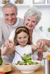 Tuinposter Smiling grandparents eating a salad with granddaughter © WavebreakMediaMicro