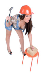 Emotional young woman in orange helmet hammer in nail