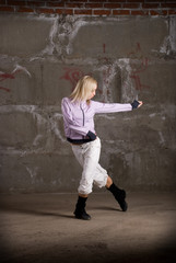 Fototapeta na wymiar Beautiful hip hop girl dancing over grey brick wall
