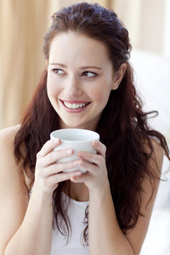 Beautiful woman drinking a cup of coffee in bed